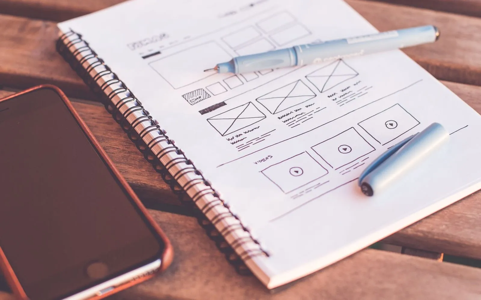 A hand-drawn website layout sketched in a notebook on a wooden table
